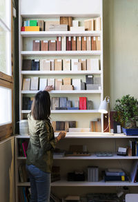 Craftswoman choosing wooden sample from shelf in workshop