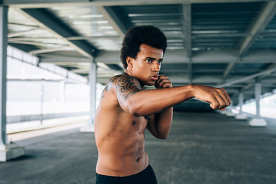 Shirtless male boxer exercising below bridge