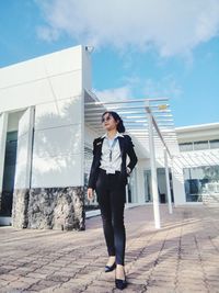 Portrait of young woman standing on footpath against sky