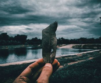 Close-up of hand holding water against sky