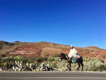 Man riding motorcycle on road against clear blue sky