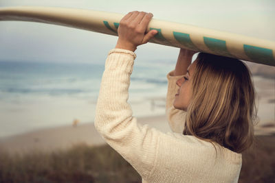 Woman carrying surfboard over her head at beach