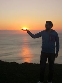 Silhouette man standing on shore against sky during sunset