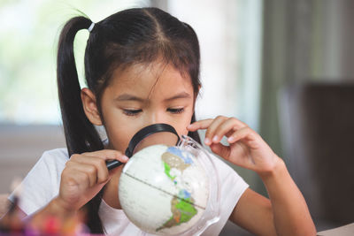 Girl looking at globe through magnifying glass in classroom