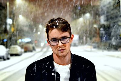 Close-up portrait handsome young man standing on road during snowfall