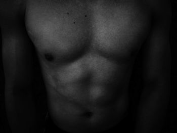 Midsection of shirtless man standing against black background