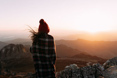 Rear view of person looking at rock against sky during sunset