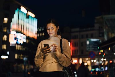 Woman using smart phone in city at night