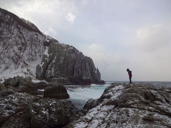 Man standing on rock by sea against sky