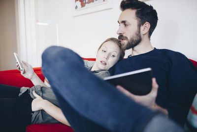 Couple using technologies while sitting on sofa in living room at home
