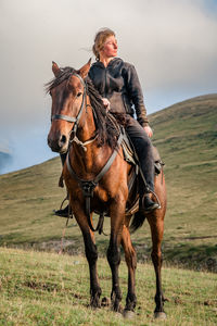 A cowgirl shepherd rider on a horse gallops through a mountain valley on autumn day sky with clouds