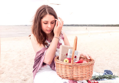 Beautiful young woman wearing sunglasses on sand at beach against sky