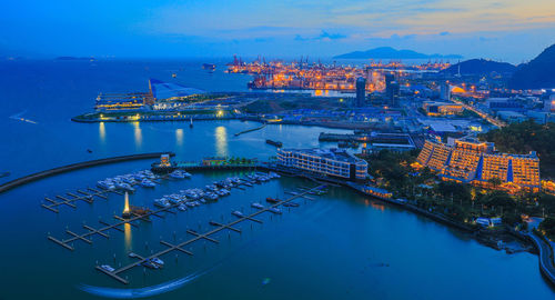 High angle view of illuminated city by sea against sky