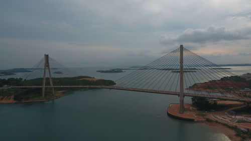 Suspension bridge over river against cloudy sky