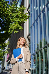 Portrait of young woman standing against building