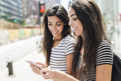 Usa, new york city, two happy twin sisters looking at cell phones in manhattan