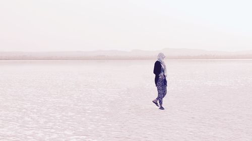 Woman standing in calm sea against mountain range