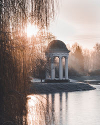 Built structure by lake against sky during sunset