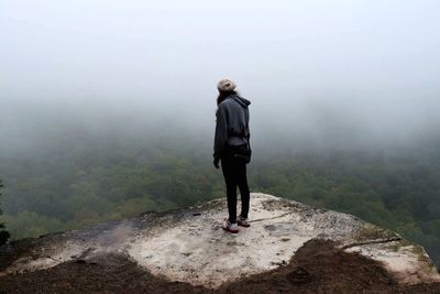 Rear view of woman standing on mountain in foggy weather