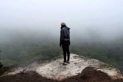 Rear view of man standing in front of mountains in foggy weather