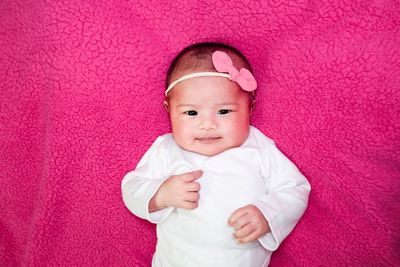 Portrait of cute baby girl lying down on pink bed