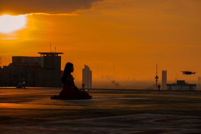 Rear view of woman sitting on street against sky during sunset in jakarta 