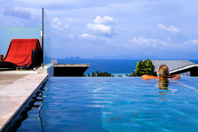 Rear view of woman in infinite pool against sky