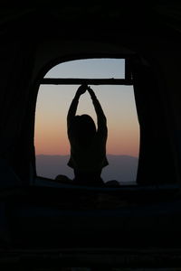 Silhouette man standing by window at sunset