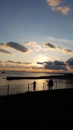 Silhouette people on beach against sky during sunset