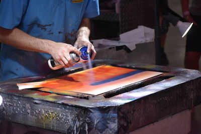 Midsection of artist spray painting at workshop at art studio