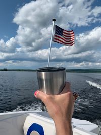 Midsection of person holding flag against lake against sky