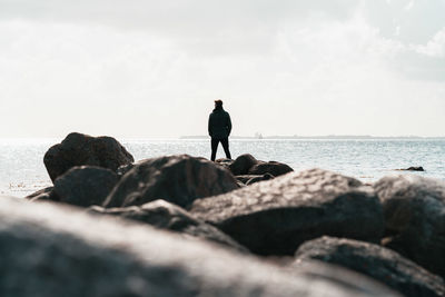 Rear view of man standing on rock by sea against sky