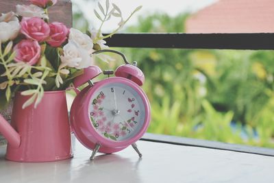 Close-up of pink alarm clock and flower vase on table at home