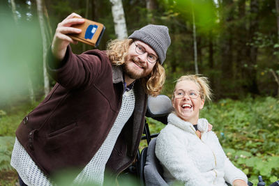 Young male caretaker taking selfie with disabled woman in forest