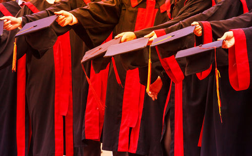 Midsection of graduates holding mortarboards