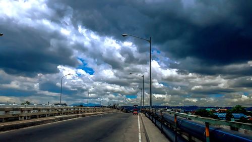 Vehicles on road against cloudy sky