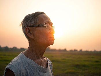 Senior man looking away while standing against sky during sunset