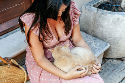 Woman in pink dress petting a ginger cat.