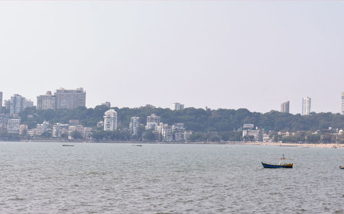 Sailboats in sea by buildings against clear sky