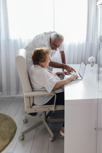 Man explaining laptop to senior woman at home