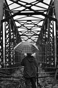 Rear view of man walking on wet bridge during rainy season