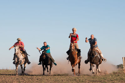 People riding horses on field against clear sky