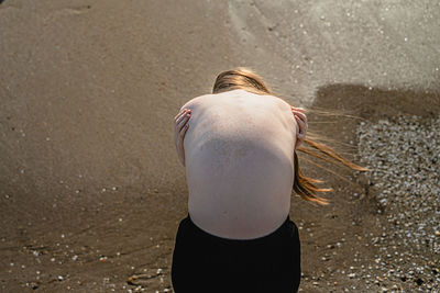 High angle view of shirtless woman hugging self at beach
