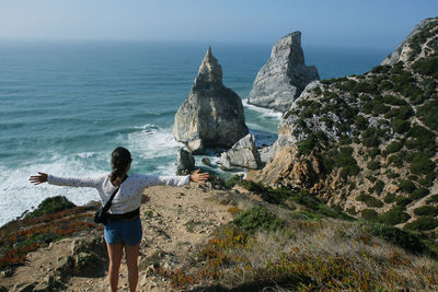 Rear view of woman with arms outstretched standing against sea