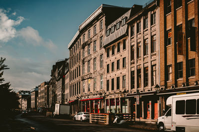 Cars on road by buildings against sky in city