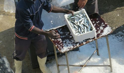 High angle view of fisherman with fish in box by ice crushing machine at harbor