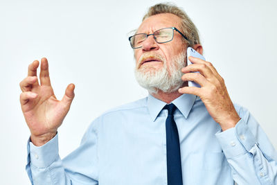 Frustrated senior man talking on phone against white background