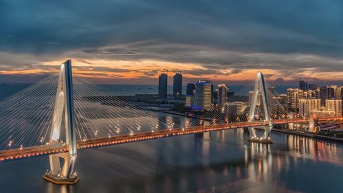 Suspension bridge over river in city during sunset