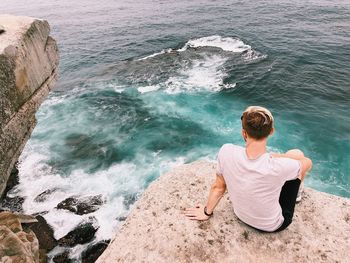 Rear view of man sitting on rock by sea