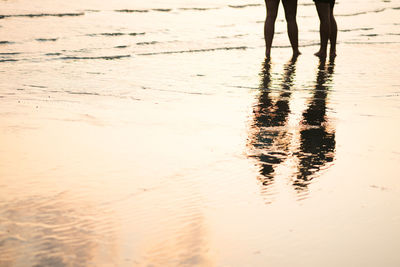 Low section of silhouette women standing on shore at beach during sunset